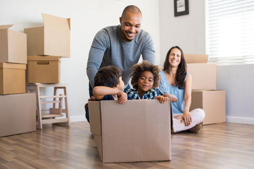 Happy African American father playing with children sitting in a cardboard box at their new home.