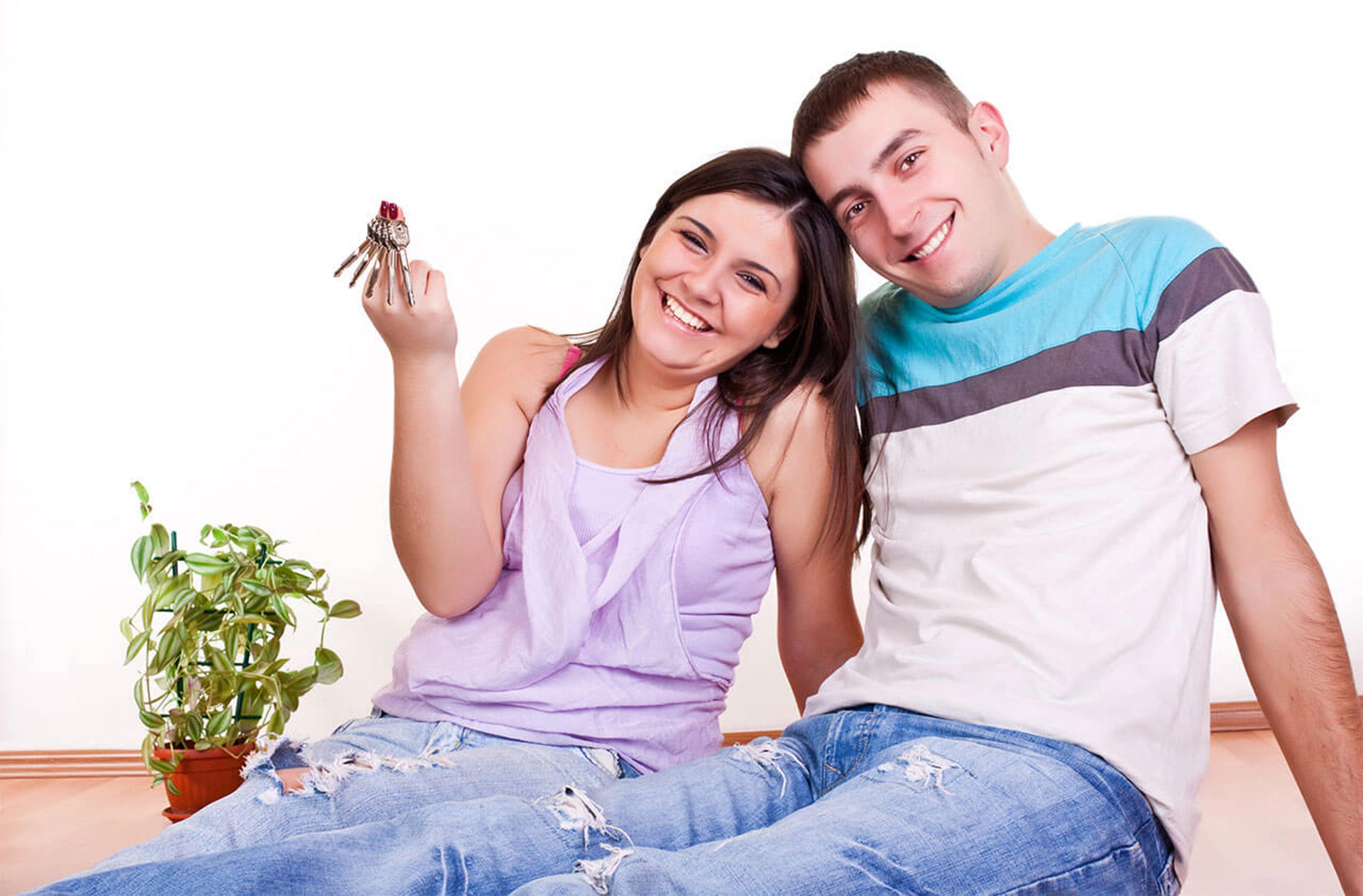 A young happy couple sitting side by side with big grins holding up a set of house keys.  Represents Housing Services for the feedback page.