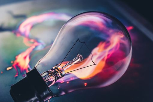 A light bulb laying on a dark table with what appears to be pink and orange fire trailing behind it.